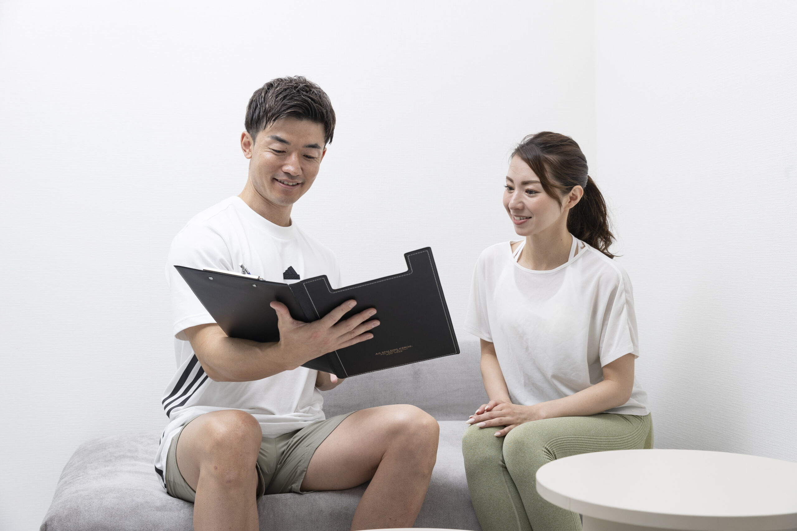 30代以降の女性がパーソナルトレーナーと一対一で、体の悩みや目標についてカウンセリングを受けている様子