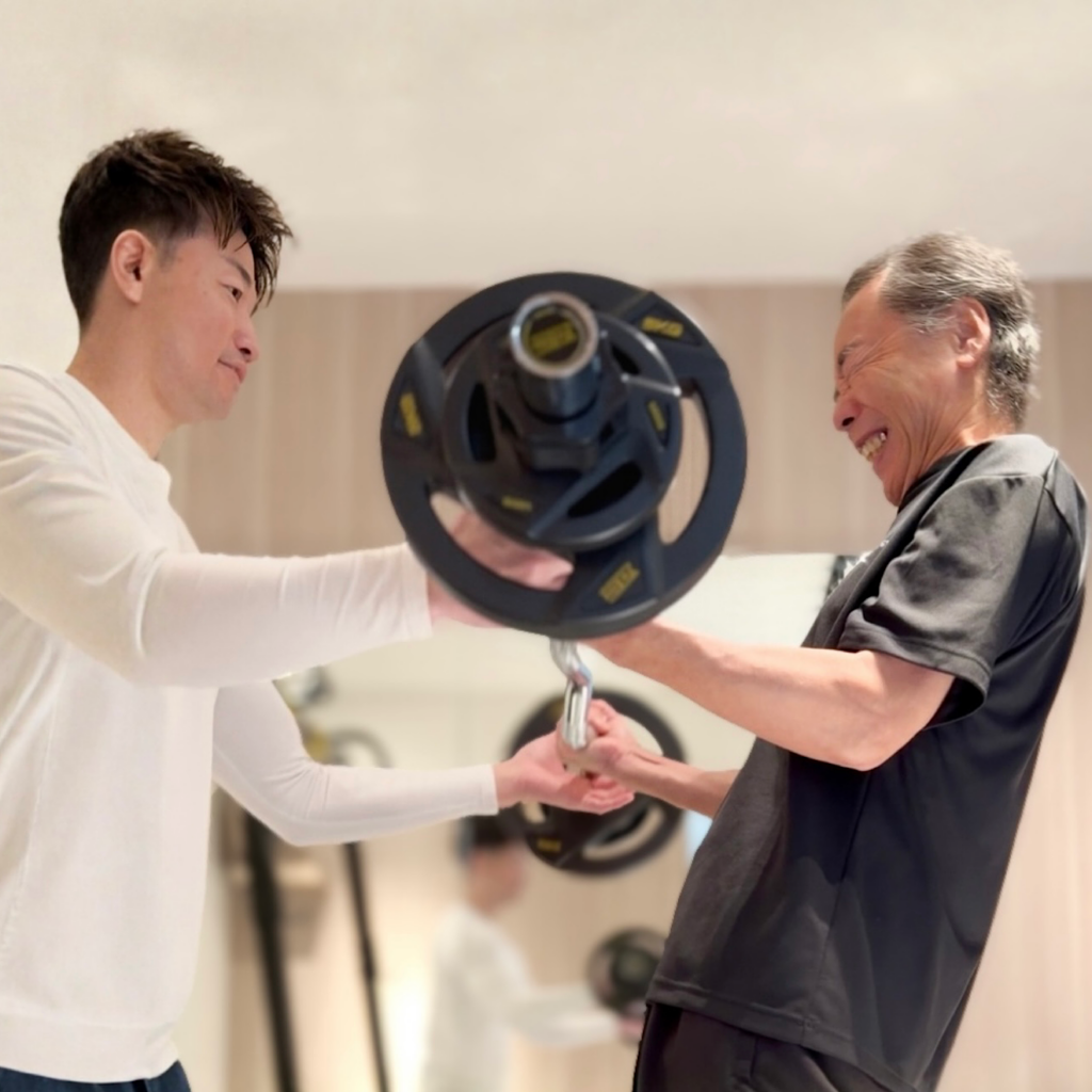 60代の男性がマンツーマン指導で、安全に配慮しながら筋力トレーニングに取り組んでいる様子