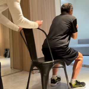 70代の男性がマンツーマン指導で、安全に配慮しながら椅子スクワットに取り組んでいる様子